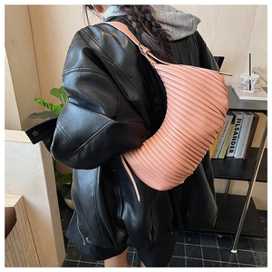 Détail du sac croissant plissé rose avec fine bandoulière porté sur une veste en cuir