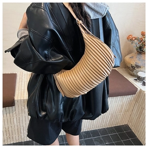 Détail de la texture du sac croissant beige plissé avec une veste en cuir noir