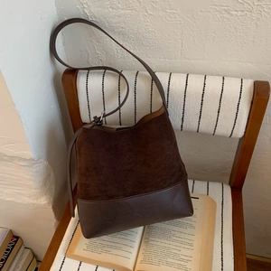 Sac seau vintage en daim marron foncé et cuir lisse suspendu sur une chaise