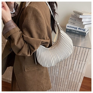 Détail du sac croissant plissé crème porté avec un blazer en velours côtelé marron
