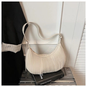 Détail du sac demi-lune plissé crème avec textures verticales sur une valise noire