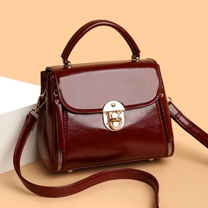 Vintage burgundy leather handbag with gold lock and adjustable strap on white pedestal