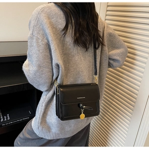 Detail shot of a black minimalist leather bag with golden pendant on a model in gray knitwear