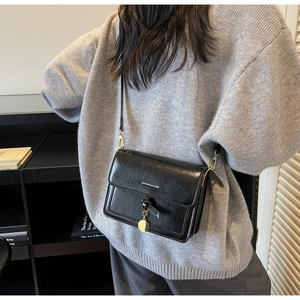 Detail view of black square crossbody bag featuring gold charm and engraved lettering