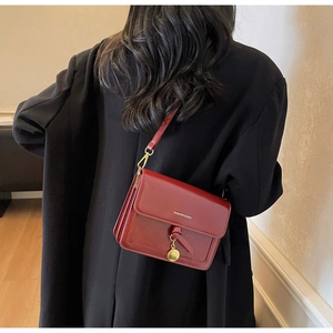 Detail of red leather square bag with fashion lettering and gold pendant charm