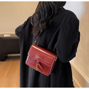 Detail of dark red oil-wax leather crossbody bag with knot pendant and gold accents