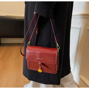 Detail of red rectangular crossbody bag featuring a golden disc pendant and embossed text