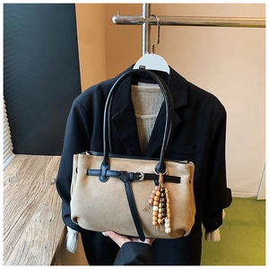 Detail of khaki frosted tote bag with black leather handles and ethnic wood bead charm
