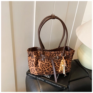 Close-up of leopard print tote bag on books featuring wooden bead charm and metal buckle