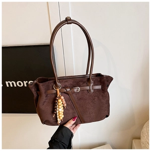 Detail of dark brown suede shoulder bag featuring decorative buckle and wooden bead charm