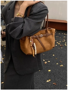 Detail of vintage brown suede tote bag with leather buckle strap and wooden bead charm