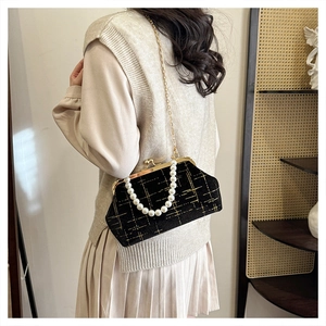 Detail of a black quilted shell bag with pearl handle and golden chain on a model