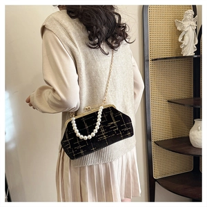 Detail of elegant black shell bag featuring golden lattice pattern and large pearl handle strap