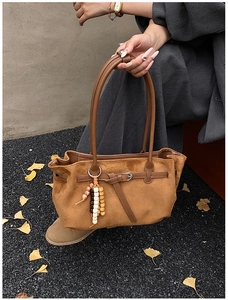 Caramel brown suede dumpling bag with wooden bead charm in an autumn street setting