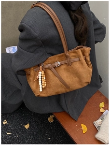 Detail of a brown suede hobo bag featuring silver buckle and stylish beaded charm