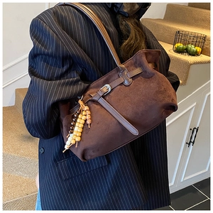 Detail of dark brown faux suede handbag with a silver metal buckle and beaded charm
