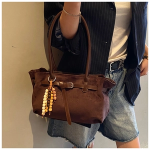 Detailed view of a brown suede dumpling bag with vintage buckle and ethnic beaded tassel
