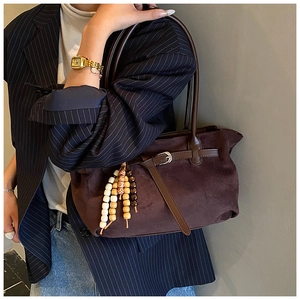 Detail of a dark brown suede dumpling bag featuring wooden beads and buckle detail