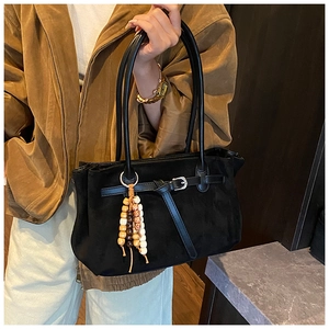 Close-up of black matte suede tote bag with a wooden bead charm and long shoulder strap