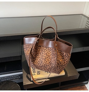 Close-up detail of leopard print canvas tote bag with brown leather handles on a shelf