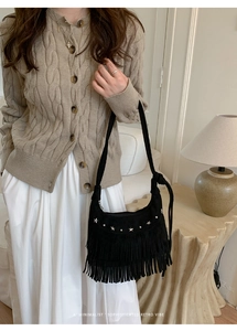 Detail of black suede shoulder bag featuring silver star rivets and long fringe tassels