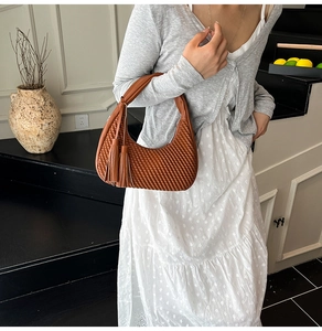 Dettaglio borsa hobo marrone a pieghe con nappine sfrangiate in un contesto lifestyle
