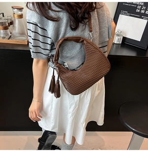 Dettaglio di una borsa hobo intrecciata marrone con doppie nappe decorative e look da strada