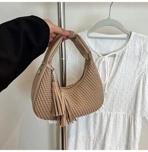 Dettaglio della borsa a mano intrecciata color cammello con nappe e manico in pelle liscia