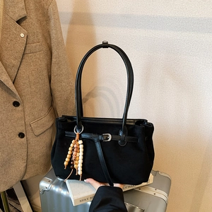 Black frosted suede dumpling bag with decorative wood beads on a metallic suitcase