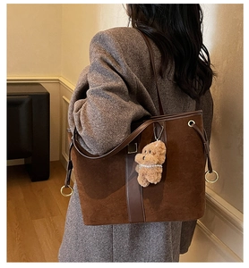 Close-up of a large brown suede tote bag with golden hardware and plush bear charm