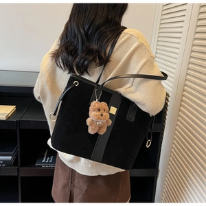 Detail of large black suede tote bag with leather trim and brown teddy bear charm