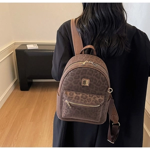 Leopard print backpack with gold hardware shown on person in a stylish interior