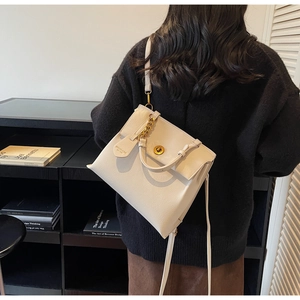 Détail du sac à bandoulière en cuir crème avec boucles dorées porté par un modèle