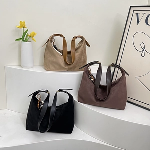 Three large suede shoulder bags with wooden bead charms on a minimalist display stand