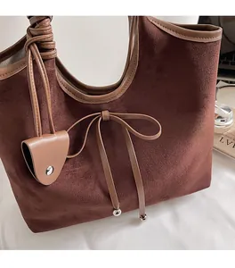 Detail view of dark brown suede tote bag with leather bow and metallic charms
