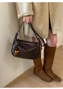 Close-up of a brown leather crescent shoulder bag with unique colorful wooden bead charm