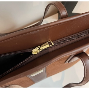 Detail of dark brown leather tote with suede panels and polished gold zipper hardware