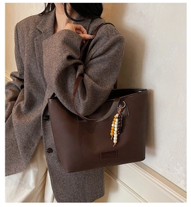 Detail of dark brown tote bag featuring colorful bead charm and textured synthetic leather