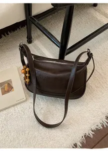 Detail of dark brown dumpling bag with pleated texture and ethnic wooden bead charm