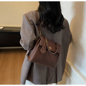 Détail du sac vintage en cuir marron avec fermoir doré et bandoulière sur une veste grise
