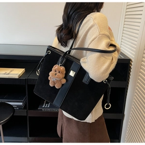 Detail of black patchwork tote bag with metal square and plush bear charm on shoulder