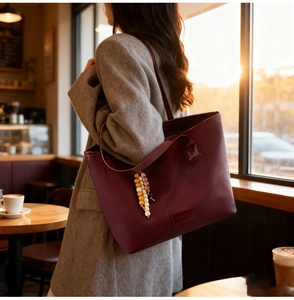 Close-up of a burgundy leather tote bag with a colorful beaded charm in a warm cafe
