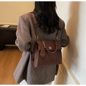 Détail du sac à dos rétro en cuir marron avec fermoir doré porté sur une veste grise