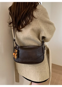 Detail of a dark brown retro hobo bag with colorful wooden beads on a beige coat