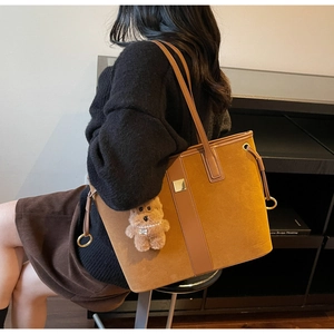 Detail of tan suede tote bag with leather trim and plush bear charm on model