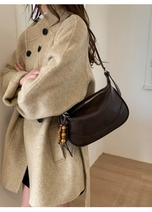Brown hobo crossbody bag with wooden bead tassel shown worn on a model's shoulder