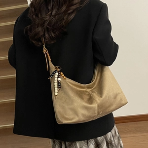 Detail of a large brown suede shoulder bag with tricolor beaded charm on a blazer