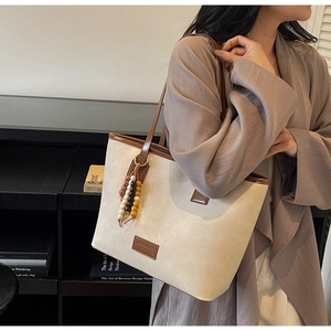 Detail of canvas tote bag with brown leather trim and colorful wooden bead tassel accessory