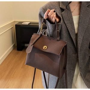 Détail du sac à main vintage en cuir marron avec boucle dorée sur un tailleur gris chic