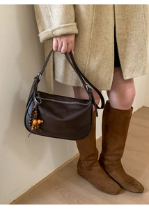 Detail view of dark brown leather crescent bag with retro wooden bead charm and metal zipper
